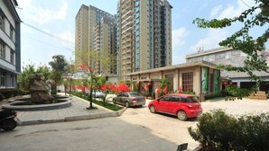 A residential area with high-rise buildings, a central roundabout, and a red car parked in front of a building with a green sign.