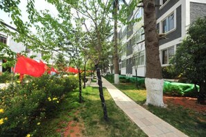 A pathway lined with trees and bushes, leading to a building with multiple windows. - Youjia Inn (Shilin)