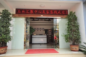 A hotel entrance with a reception desk, potted plants, and a red mat. - Youjia Inn (Shilin)