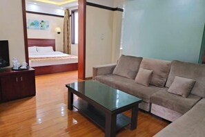 A hotel room with a bed, a sofa, a glass-top table, and a wooden cabinet.