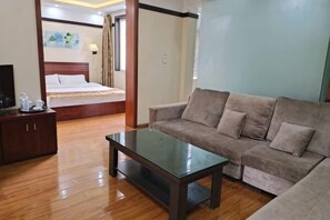 A hotel room with a bed, a sofa, a coffee table, and a TV.