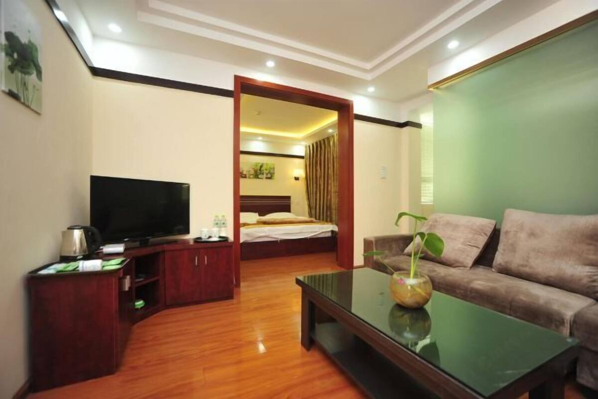 Habitación de hotel con televisión, cama, sofá, mesa de centro y escritorio pequeño con lámpara.