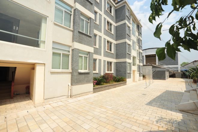 A multi-story residential building with a paved courtyard, large windows, and a covered outdoor area.