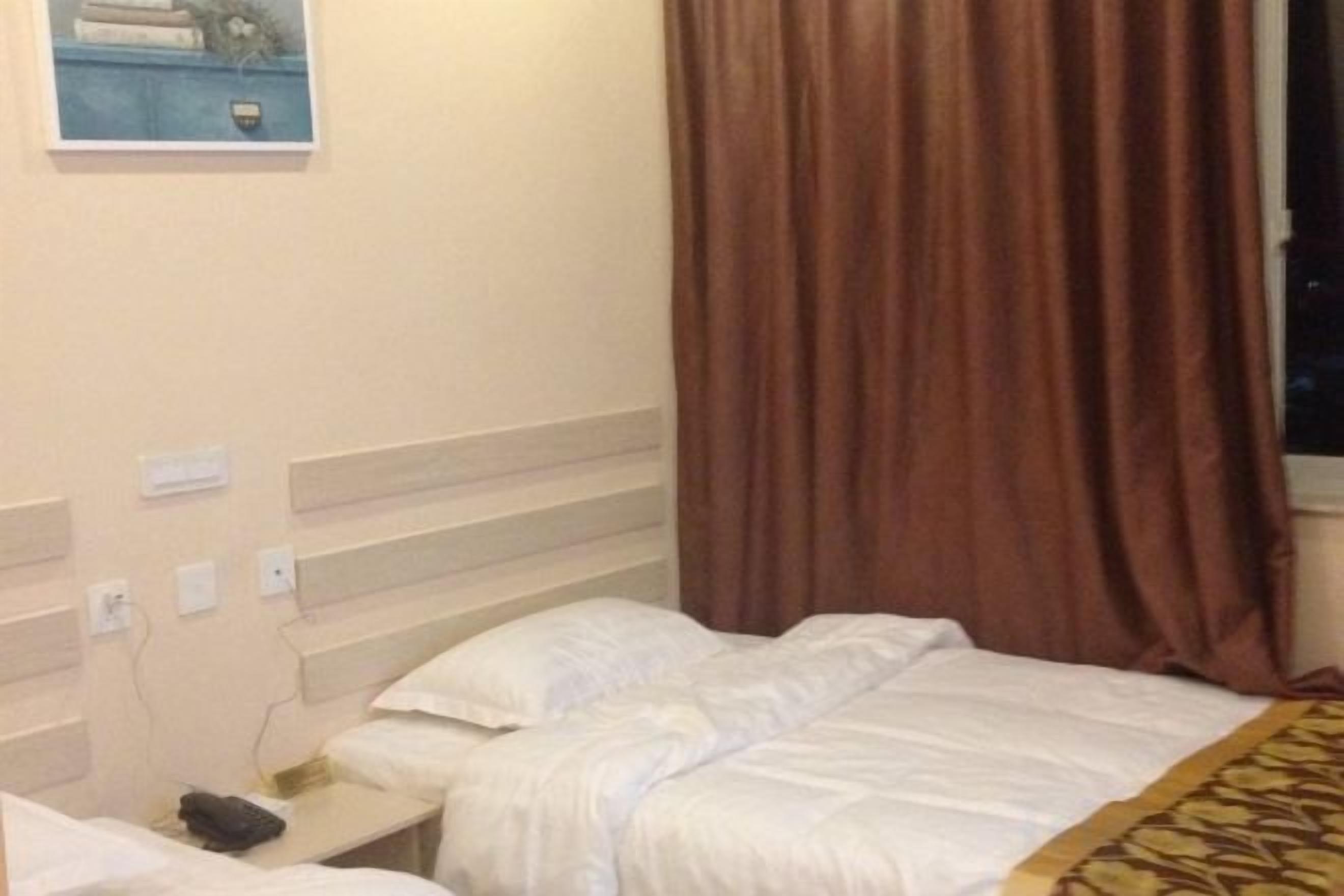 A hotel room with a bed, a bedside table, and a window with curtains.