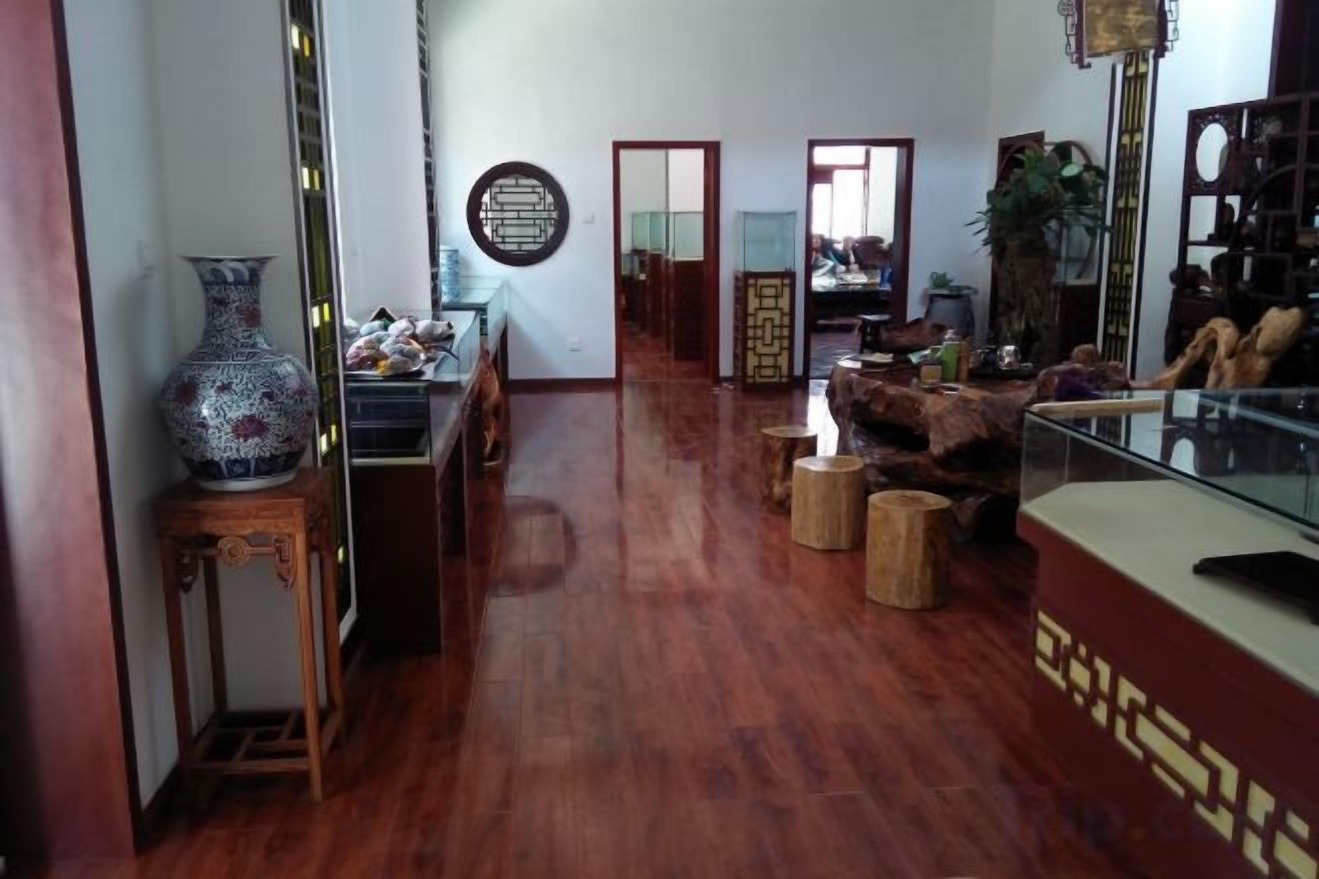 A spacious living area with a wooden floor, a large vase on a side table, and a glass display case.