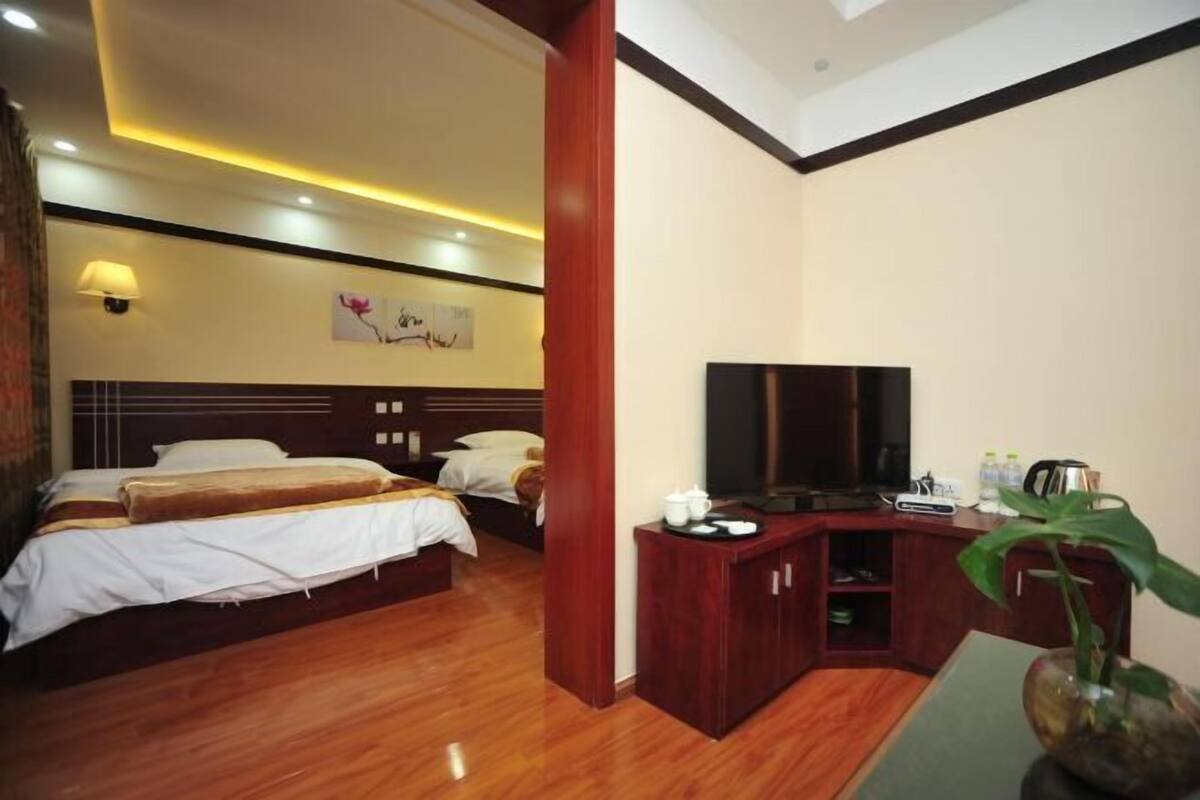 Una habitación de hotel con cama, escritorio con televisor, planta y lámpara de pared.
