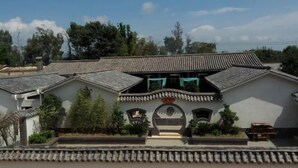 A traditional building with a tiled roof, a central entrance with a decorative arch, and a small balcony with a hanging object.