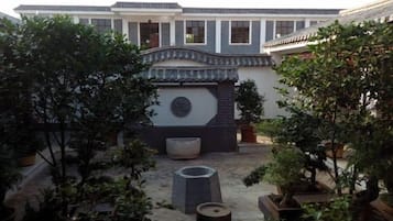 A courtyard with traditional architecture, including a tiled roof and a stone wall with a circular emblem. There are potted plants and a stone bench.