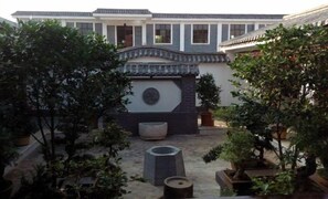 A courtyard with traditional architecture, including a tiled roof and a stone wall with a circular emblem. There are potted plants and a stone bench. - Youjia Inn (Shilin)