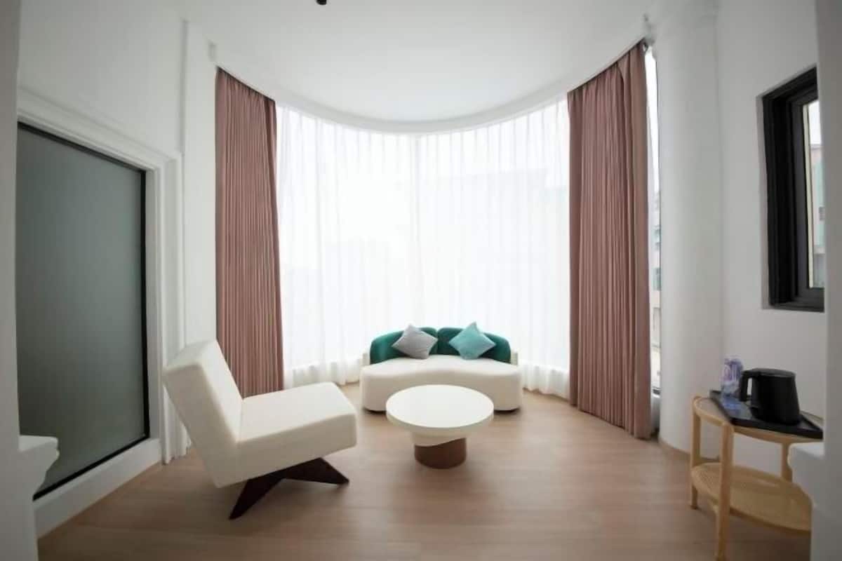 A modern living room with a white sofa, a round coffee table, and a green sofa with cushions.