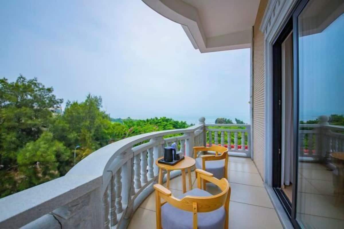 A balcony with two wooden chairs and a small table, overlooking a lush green landscape and the sea.
