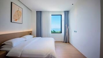 Quarto de hotel moderno com uma cama grande, vista para o exterior e um quadro na parede.