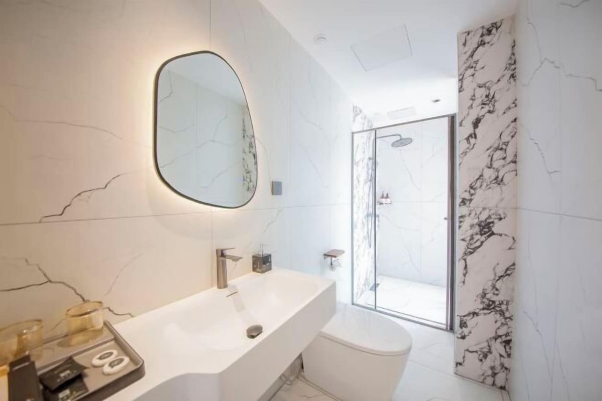 Un bagno moderno con un ampio specchio, un lavandino bianco e una zona doccia con tenda a motivi marmorizzati.