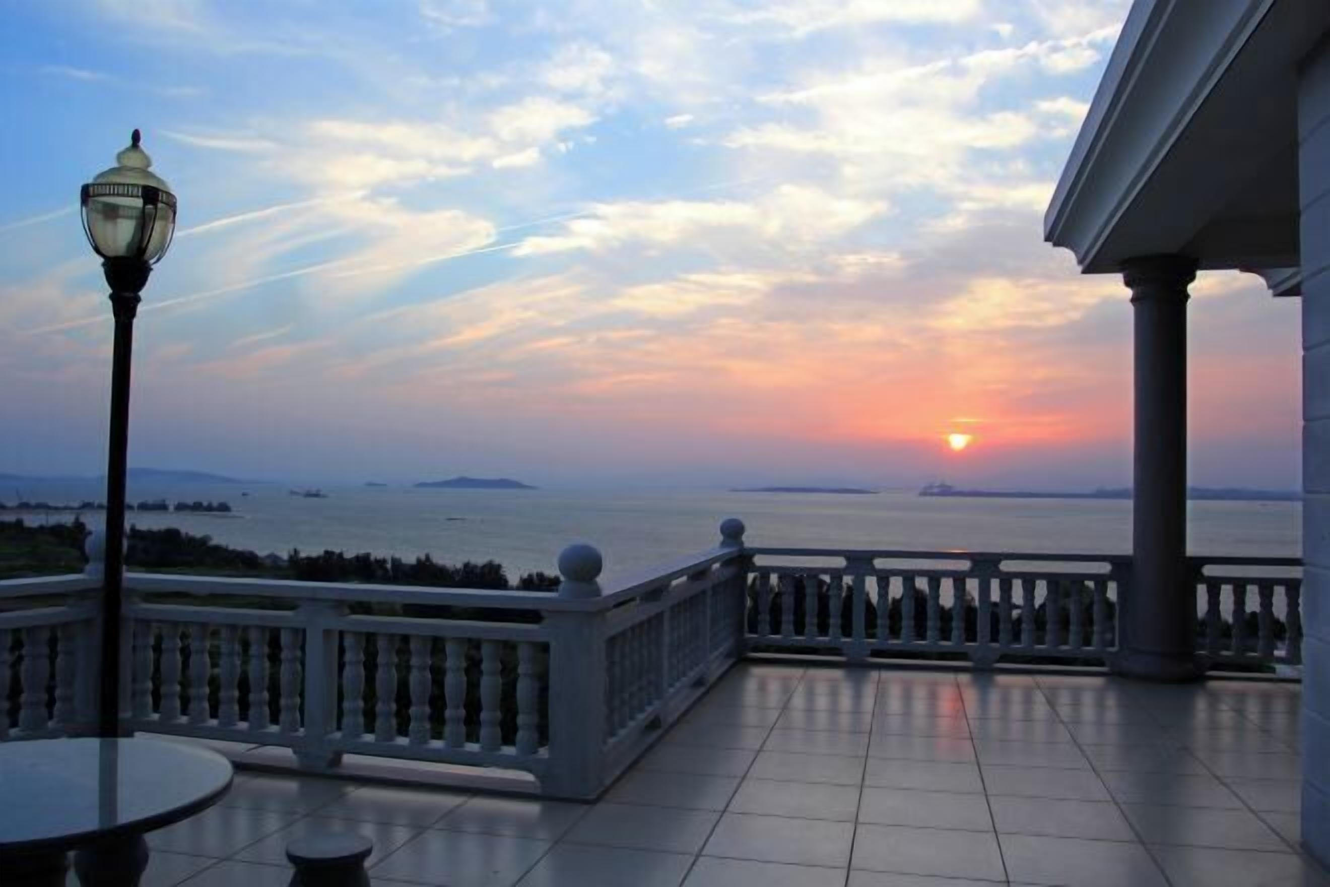 Ein Balkon mit Blick auf den Sonnenuntergang über dem Wasser, eine Laterne und ein weißes Geländer.