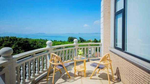 A balcony with a view of the sea, furnished with wooden chairs and a small table. - Lanting Holiday Villa (Putian)