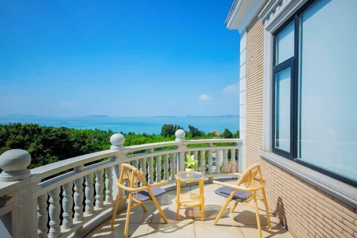 A balcony with a view of the sea, furnished with wooden chairs and a small table.