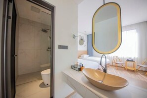 A modern bathroom with a glass shower enclosure, a large oval sink, and a bed with white linens. - Lanting Holiday Villa (Putian)