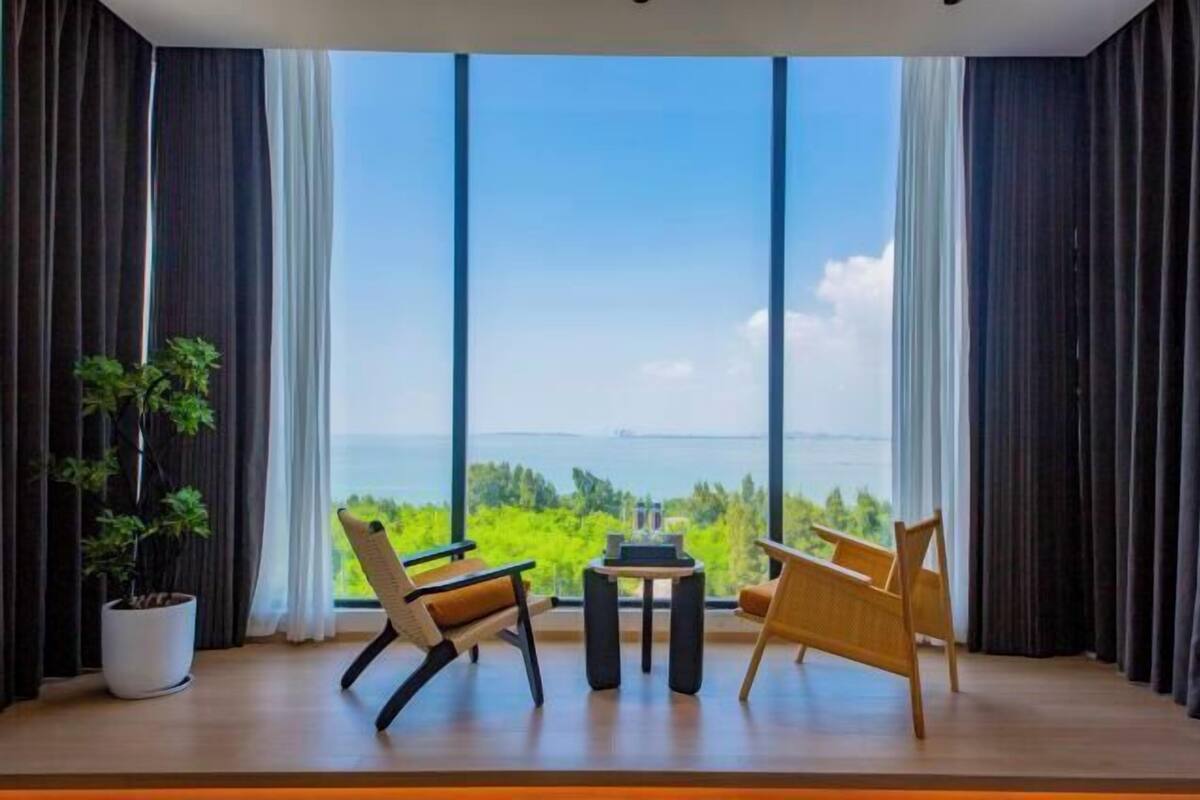 A room with large windows, a potted plant, two chairs, and a small table.