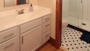 A bathroom with a large mirror, a sink with a soap dispenser, and a shower area with a glass door.