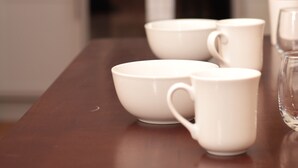 A kitchen with white cabinets, a microwave, and a wooden table with white cups.