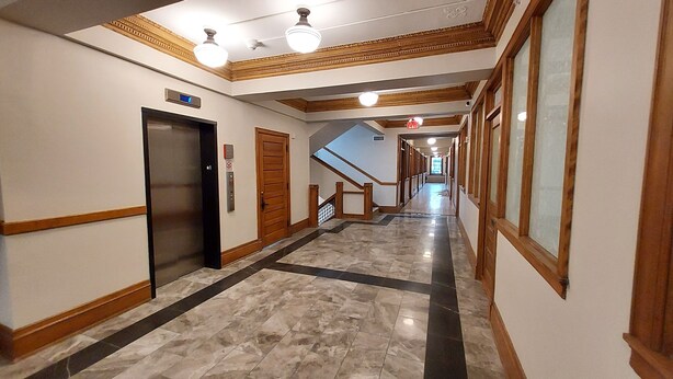 A hotel hallway with marble flooring, wooden doors, and a staircase.