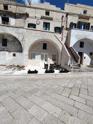 A courtyard with stone flooring, outdoor seating, and a staircase leading to an upper level.