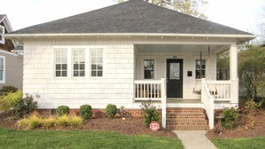 A single-story house with a front porch, a black front door, and a small front yard with a stop sign.