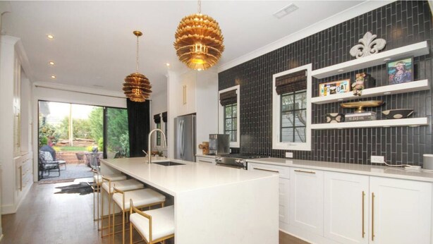 A modern kitchen with a large island, white cabinetry, and a black backsplash.