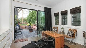 A modern dining area with a wooden table, metal chairs, and a view of the garden through large sliding glass doors.