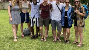A group of people standing on a grassy area with trees and a brick wall in the background. - Whispers  Guest House  (Kumasi)