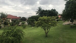A grassy area with trees and a building with a red roof. - Whispers  Guest House  (Kumasi)