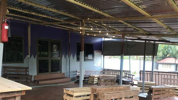 An outdoor seating area with wooden benches and tables, a covered roof, and a fire extinguisher mounted on the wall. - Whispers  Guest House  (Kumasi)