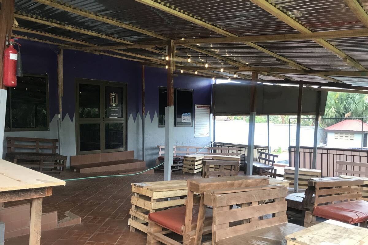 An outdoor seating area with wooden benches and tables, a covered roof, and a fire extinguisher mounted on the wall.