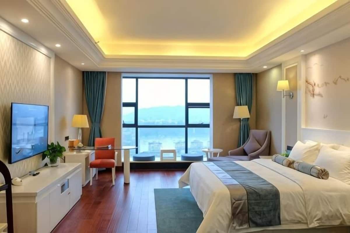 Habitación de hotel con cama, escritorio, silla, televisor y un ventanal con vistas.
