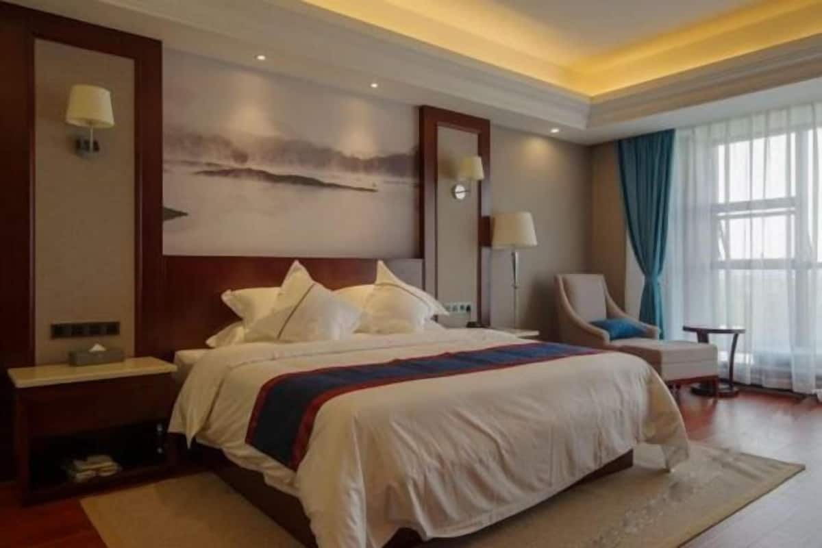 Una habitación de hotel con una cama grande, una mesita de noche, una silla, un escritorio y un cuadro en la pared.
