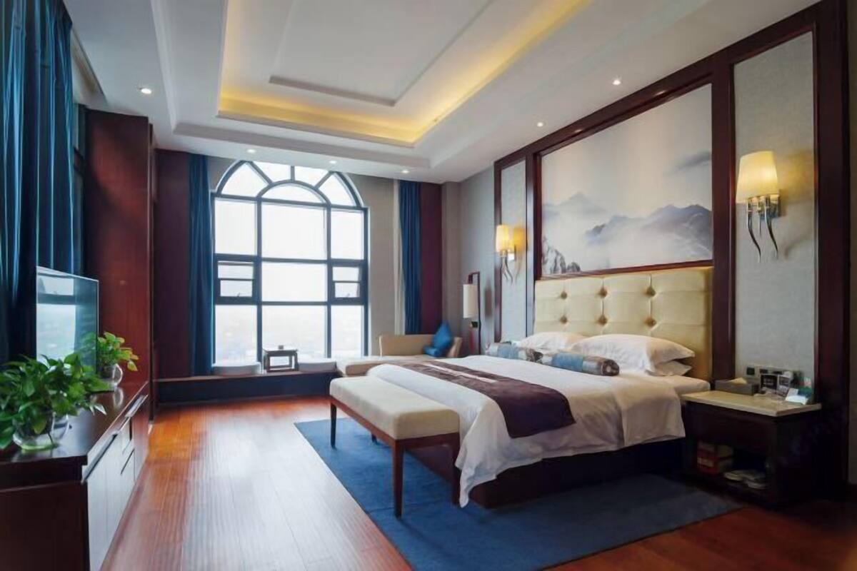 Una habitación de hotel con una cama grande, un banco, un escritorio y un televisor.