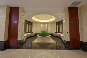Eine Hotelhalle mit einer zentralen Sitzgruppe, einem Empfangsbereich und einem großen Spiegel.