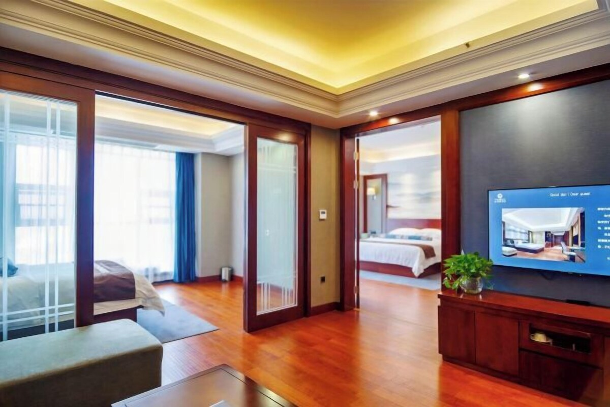 A hotel room with a television, a bed, a seating area, and a view of the outside.