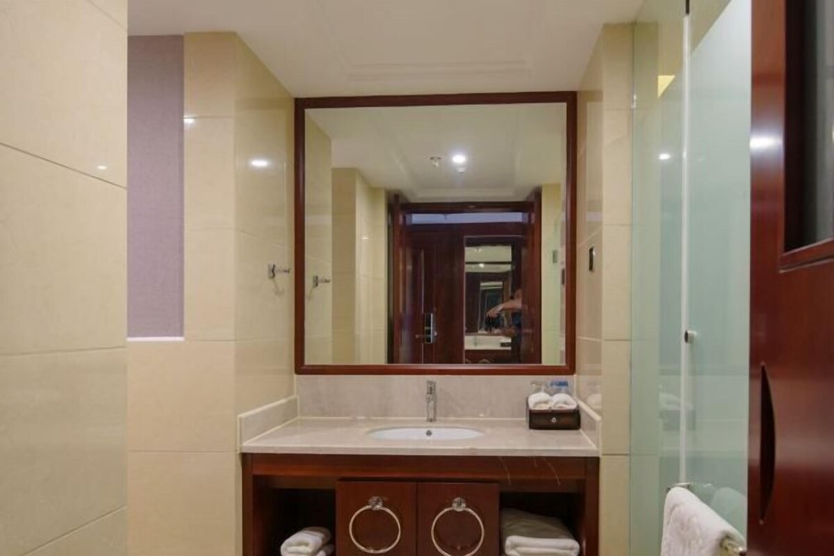 Une salle de bain dotée d’un grand miroir, d’un lavabo, d’un meuble-vasque avec deux porte-serviettes et d’une cabine de douche en verre.