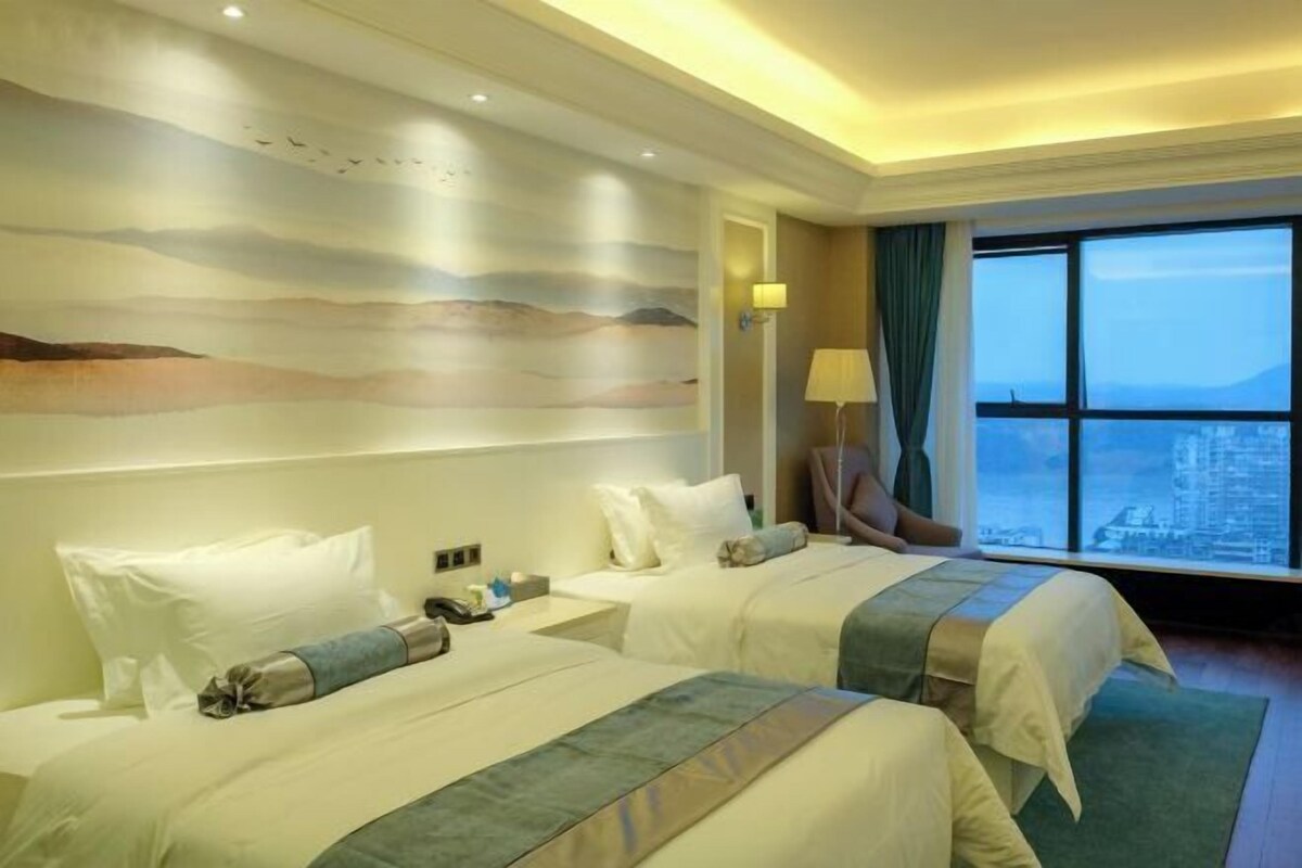 Een hotelkamer met twee bedden, een groot raam met uitzicht over de stad en een muurschildering.