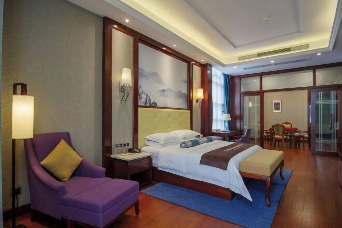 Una habitación de hotel con cama, una silla, un escritorio y un amplio ventanal.