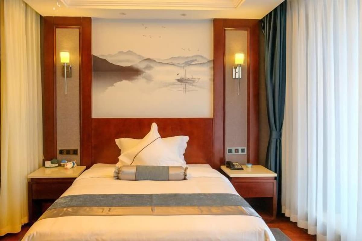 Une chambre d’hôtel avec un grand lit, deux tables de chevet, un tableau au mur et des rideaux.