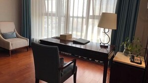 A hotel room with a wooden floor, a desk with a lamp, a chair, a small table with a phone, and a window with curtains. - Jiu Long Ying Bin Hotel (Yibin)