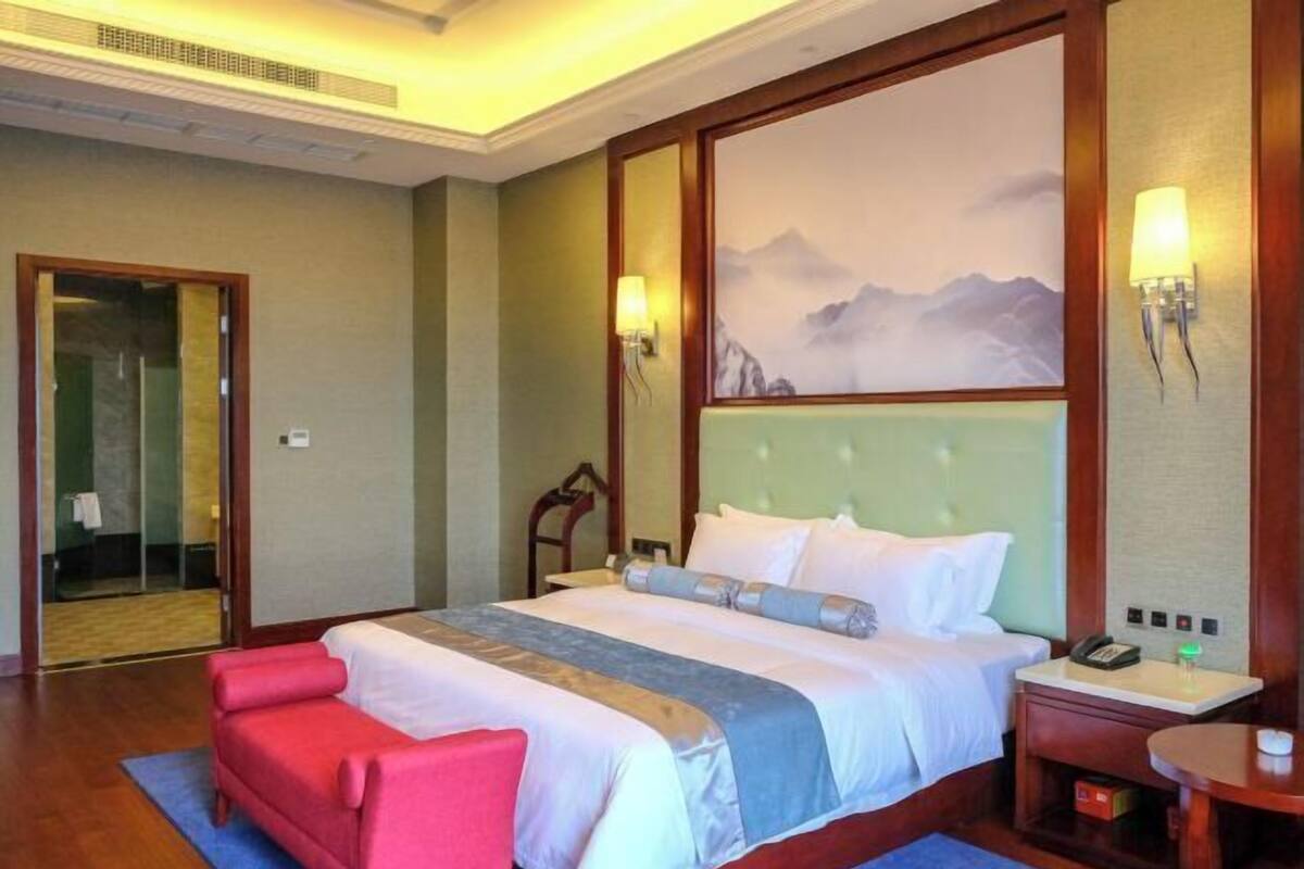Una habitación de hotel con una cama, una silla roja, una mesita de noche y un cuadro en la pared.