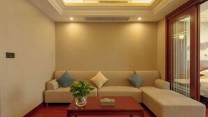 A living room with a beige sofa, a wooden coffee table, and a potted plant. - Jiu Long Ying Bin Hotel (Yibin)