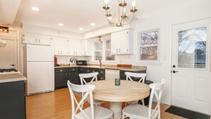 A modern kitchen with white cabinets, a central island, and a dining area with white chairs. - Cozy, Roomy Ranch near IU Stadiums (Bloomington)