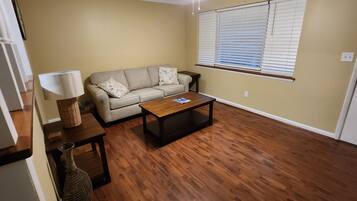 Ein Wohnzimmer mit einem beigefarbenen Sofa, einem Holztisch und einem Deckenventilator.