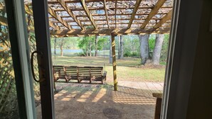 En träbänk under en pergola med utsikt över en gräsyta och träd.