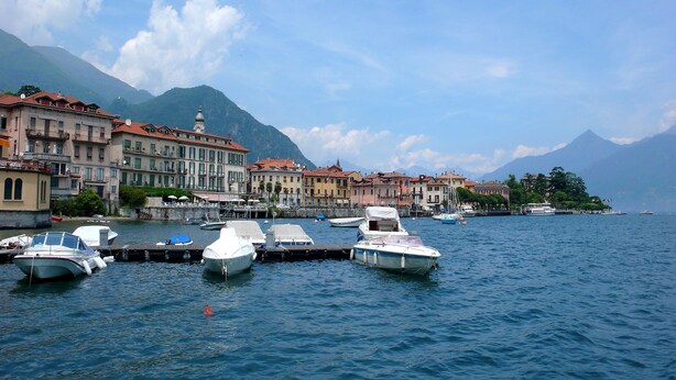 A marina with boats docked, buildings with red roofs, and mountains in the background. - Modern House Apartment 4, Menaggio, Italy (Menaggio)