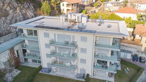 A multi-story residential building with balconies, outdoor seating, and a rooftop terrace. - Modern House Apartment 4, Menaggio, Italy (Menaggio)